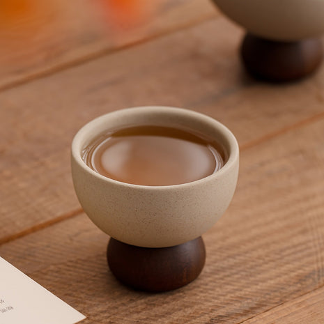 Beiger Kaffeebecher aus Steingut mit dunklem Standfuß, innen mit braunem Getränk