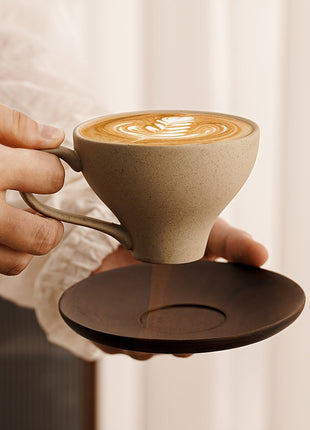 Beigefarbene Keramiktasse mit Griff, auf braunem Untersetzer