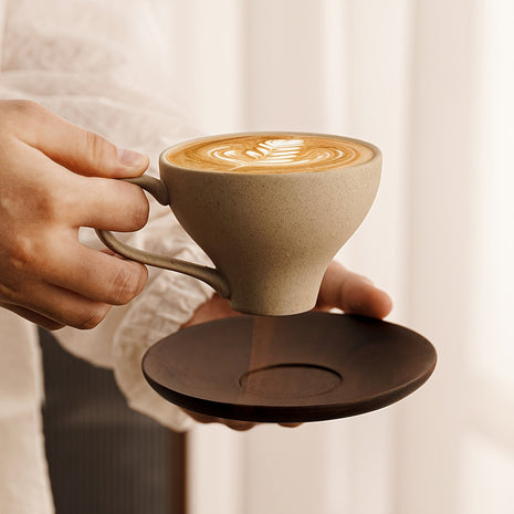 Beigefarbene Keramiktasse mit Griff, auf braunem Untersetzer