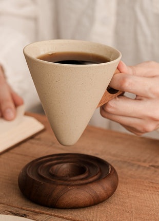 Trichterförmige Keramiktasse mit Spiralsockel aus Holz, in Hand gehalten