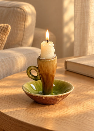Olive-green glazed ceramic chamberstick candle holder styled on a pale oak side table beside a neutral sofa